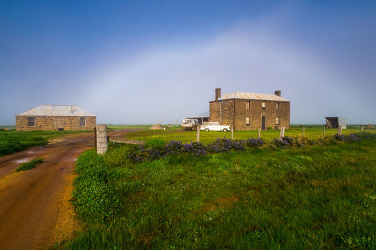 A white fog bow over old bluestone farmhouses on green farmland