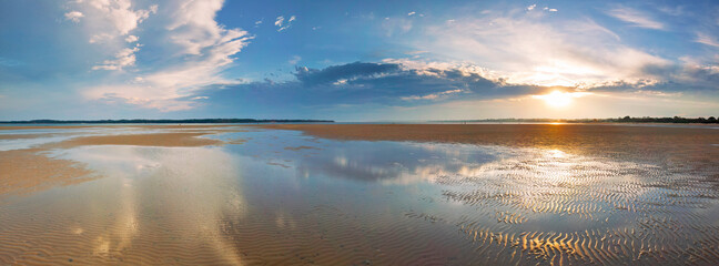 Sunset through cloud formations reflecting in pools of water on a beach