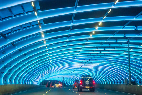 Cars on a freeway driving through a tunnel lit with coloured lights