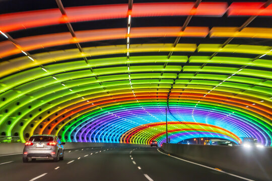 Cars on a freeway driving through a tunnel lit with coloured lights