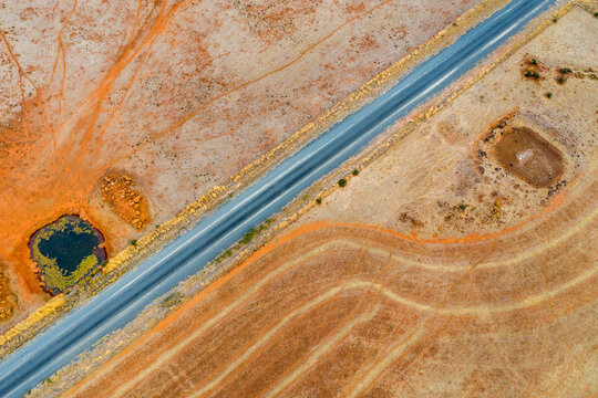 Aerial view of a country road next to a dam on dried farmland.