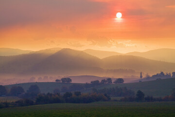 The setting sun sinks through smoke haze over a mountain range