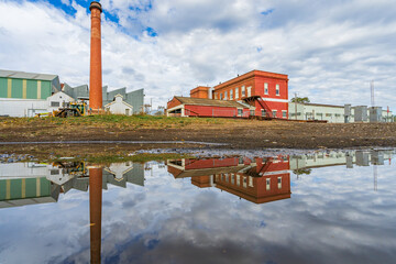 Ground level view of a brick chimney at a  factory and its reflection in a puddle