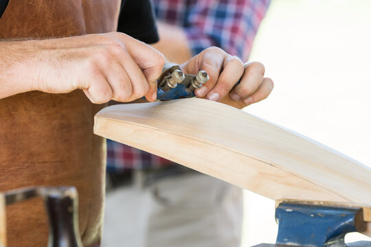 Close up of a tradesman's hands using a shaving tool over the back of cricket bat