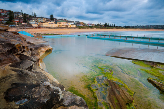 Calm waters of tidal swimming baths and a surf club building in soft predawn lighting