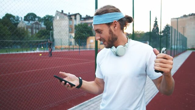 Young handsome man runner after workout training hands with espander using smartphone browsing workout application fitness tracker on the stadium.