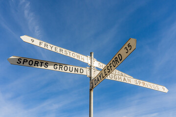 Looking up at  road sign with long directional arms, against a blue sky