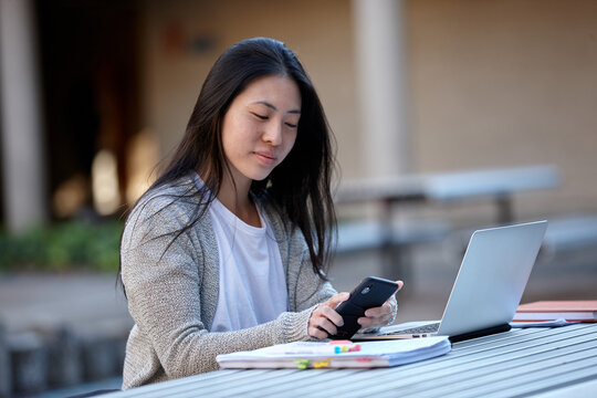 Young Asian female university student studying on laptop outdoors
