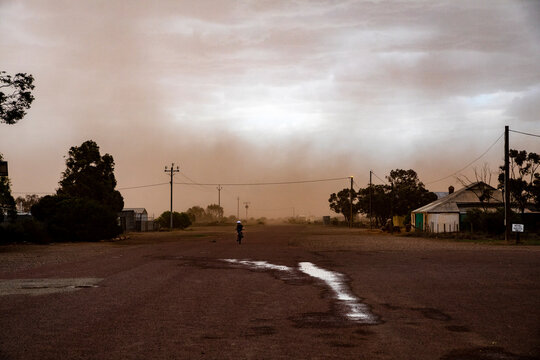 Dust storm hitting small remote town with a child riding a bike on the road