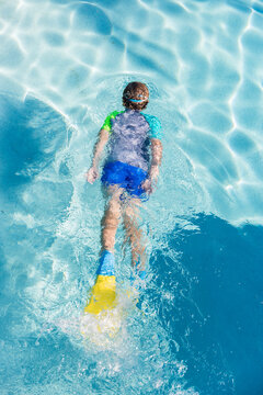 Looking down at boy wearing flippers and goggles gliding in swimming pool