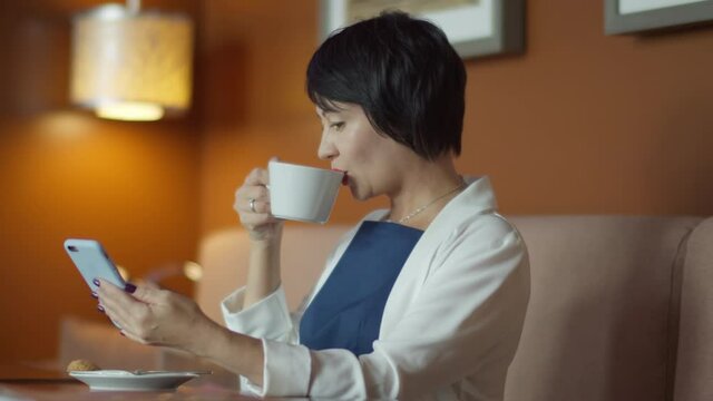business woman drinking coffee in a cafe and reading some information on the phone