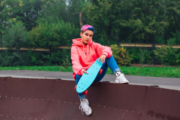 Young girl with short multicolored hair sits with skateboard in skatepark