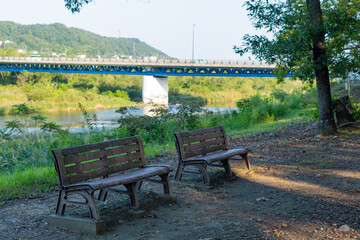 scenery of two wooden empty benches in park beside river and bridge in tokyo, japan