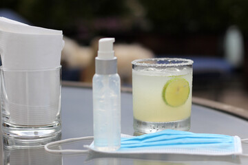 
Lemonade drink in glass on glass table, next to protection mask and antibacterial gel,
new normal covid-19
