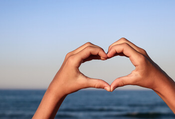 heart shape in hands.
Heart shape in hands against a background of blue sea and with a place for text on the left, side view close-up.
