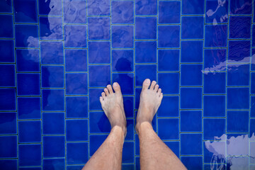 View of bare male feet standing at swimming pool side.