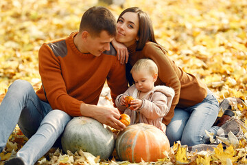 Family in a autumn park. Woman in a brown sweater. Cute little girl with parents. Family with pumpkins.