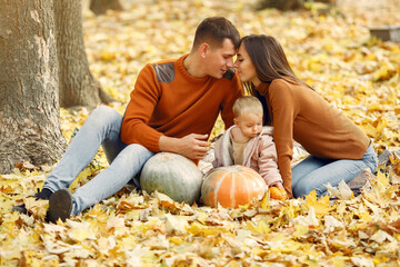 Family in a autumn park. Woman in a brown sweater. Cute little girl with parents. Family with pumpkins.