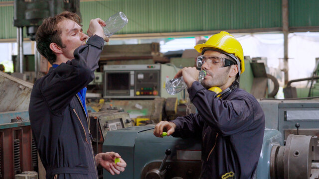 Tired Factory Workers Taking A Break And Talking To Coworker In The Factory . Industry And Engineering Concept .