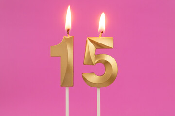 Burning golden birthday candles on pink background, number 15