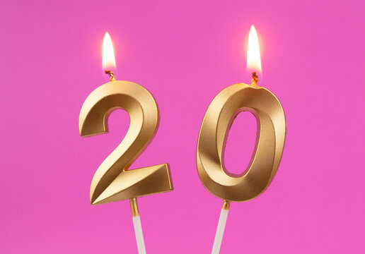 Burning golden birthday candles on pink background, number 20