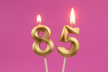 Burning golden birthday candles on pink background, number 85