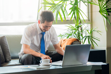 Smiling businessman analyzing data and using laptop in office.