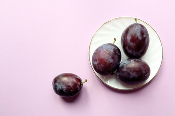 Fresh plums on and around a white saucer on a pastel background, top view, close-up, space for text
