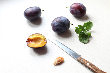 Ripe plums on the kitchen table, knife and plum slice with a stone, top view, close-up