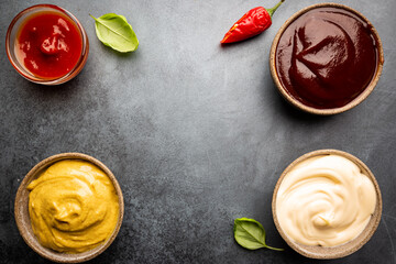 Classic set of sauces, American yellow mustard, ketchup, barbecue sauce, mayonnaise on black stone background, top view with copy space.