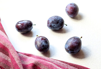 Fresh large plums on a gray surface with a kitchen napkin, side view