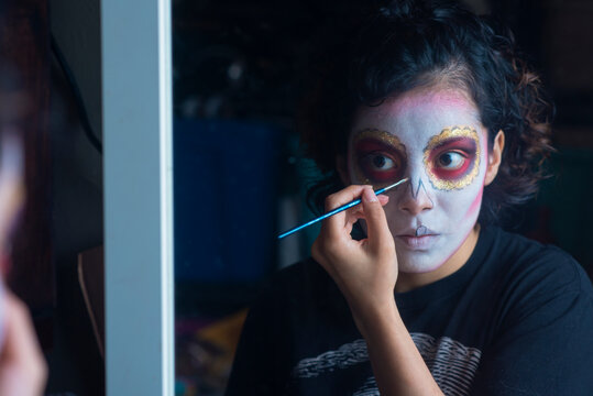 Mujer mexicana latina maquillando cara catrina calavera día de muertos tradición luz tenue, acercamiento, detalle, cuidadosa perfeccionista