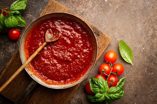 Classic homemade Italian tomato sauce with basil for pasta and pizza in the pan on a wooden chopping board on brown background, top view.