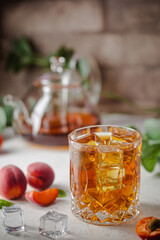 Glass of peach or apricot iced tea with fruit slices against white background