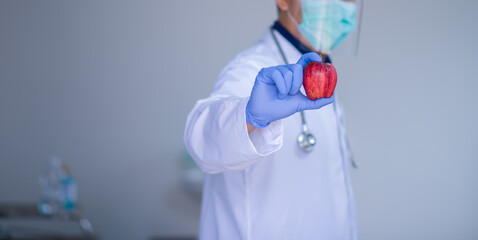 A male doctor offers a red apple ready Organic nutrition concept. Isolated front view with medicine icons on the background.