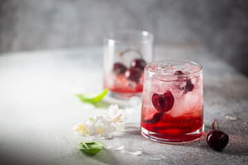 Cold cherry lemonade drink with fresh cherry and ice on gray background