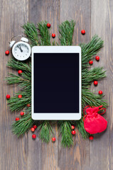 Christmas or new year background on a wooden background. Tablet with a blank screen for greetings. Flat lay, top view, copy space