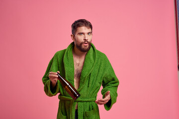 Drunk man with a bottle of alcohol in his hand on a pink background cropped view of a green robe