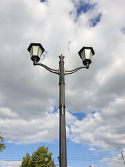 Street lamp on the background of the cloudy sky. In the town. Antique lamp. architectural European style. Street lights. Vertical photo.