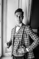 Black and white portrait guy in an elegant suit holding a watch in his hand, posing by the window.