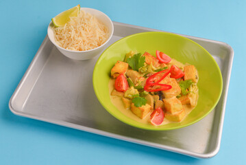 Fresh rice and chicken in gravy sauce with tomatoes, red pepper and green beans served in seperate plates on metal tray.