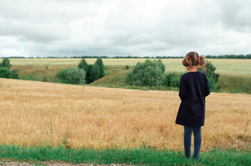 Naklejka na ściany i meble Child girl standing in a wheat field and looking into the distance. Copy space.