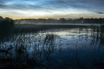 night landscape with white silver clouds over the lake, blurred foreground, charming cloud reflections in the lake water, summer night