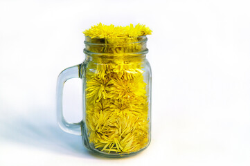 Fragrant yellow flowers are collected and lie in a glass mug on a white background. Transparent mug with plucked wildflowers