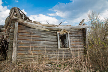 Old rustic wooden log house destroyed, without a roof against a blue sky with white clouds. Rural scene, olden time
