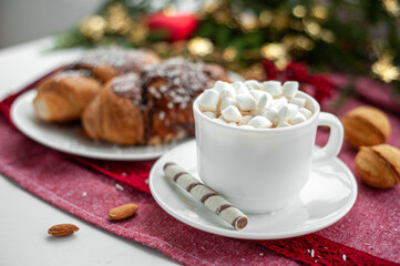 Christmas breakfast. Christmas morning. A cup of coffee or cocoa with marshmallows and sweets. On a red tablecloth next to a branch decorated with Christmas tree. Selective focus.