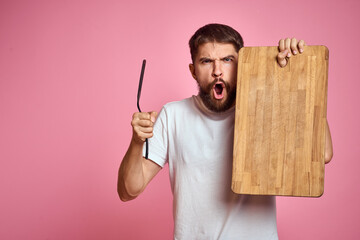 guy holding kitchen board and spatula in hand on pink background cropped view