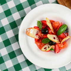 Summer salmon salad with strawberry, tomato, olives and basil in a white plate. Traditional Italian cuisine concept.