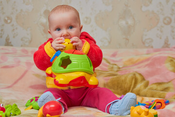 baby bites a toy,the baby bites the first teeth of a plastic toy on the bed