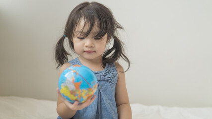 Happy playful toddler looking at globe ball on bed in bedroom at home.